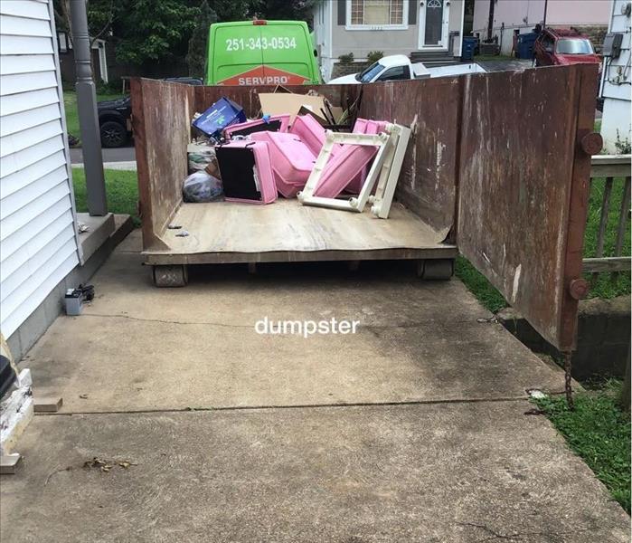 metal trash dumpster open filled with unsalvageable home furnishings