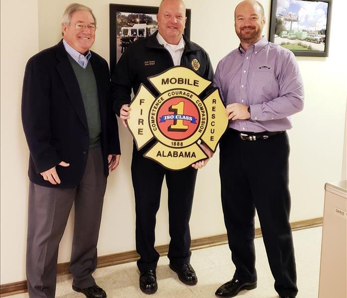 3 males smiling for the camera holding fire department shield