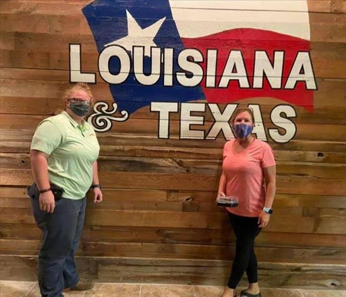 two females standing in front of wall with painting of flag and words Texas and Louisiana on it