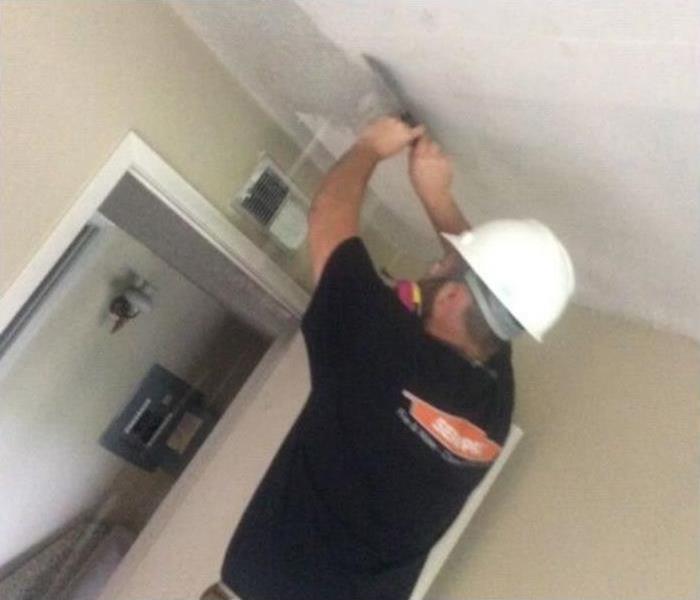 man with short sleeve black shirt with SERVPRO logo adding white plaster to a ceiling